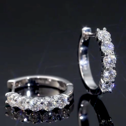 Pair of silver hoop earrings with clear gemstones on a reflective black surface.